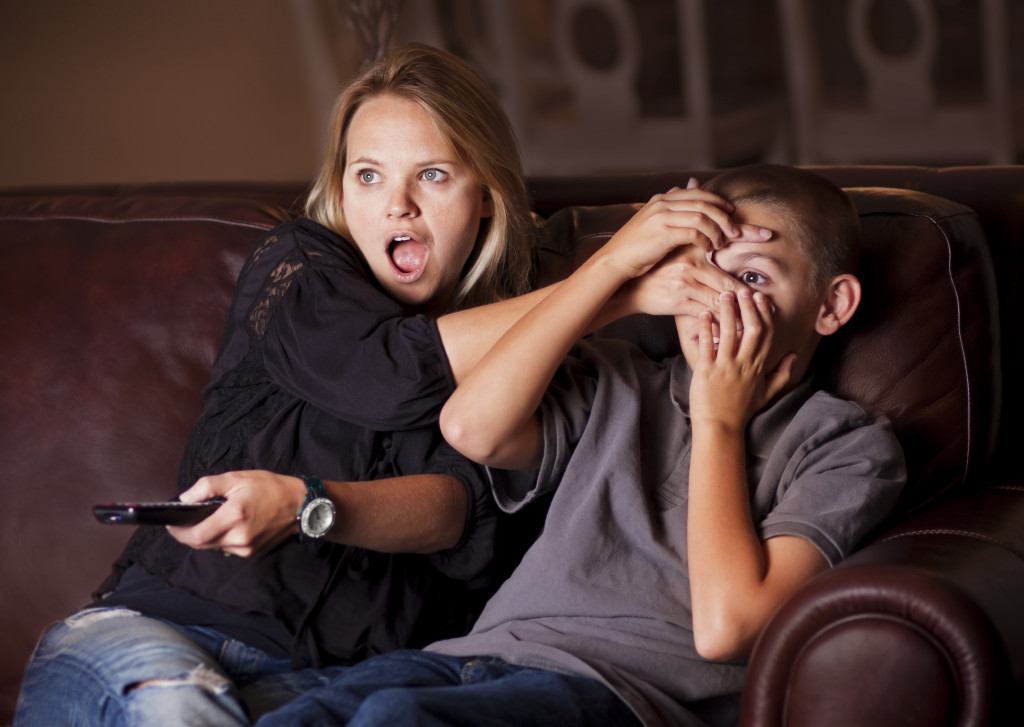older woman covering eyes of a minor while watching a scary movie